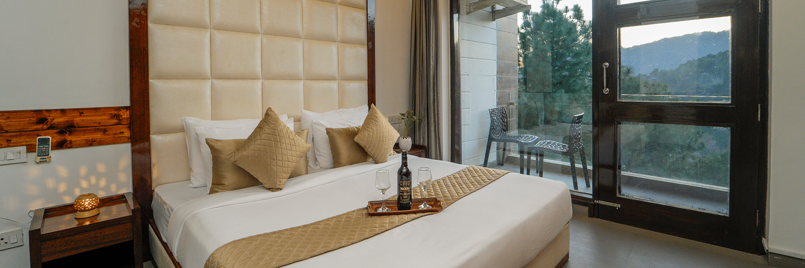 The premium room of DLS Whispering Winds with a bed, bed side tables, and a glass door leading to the balcony overlooking the mountain view